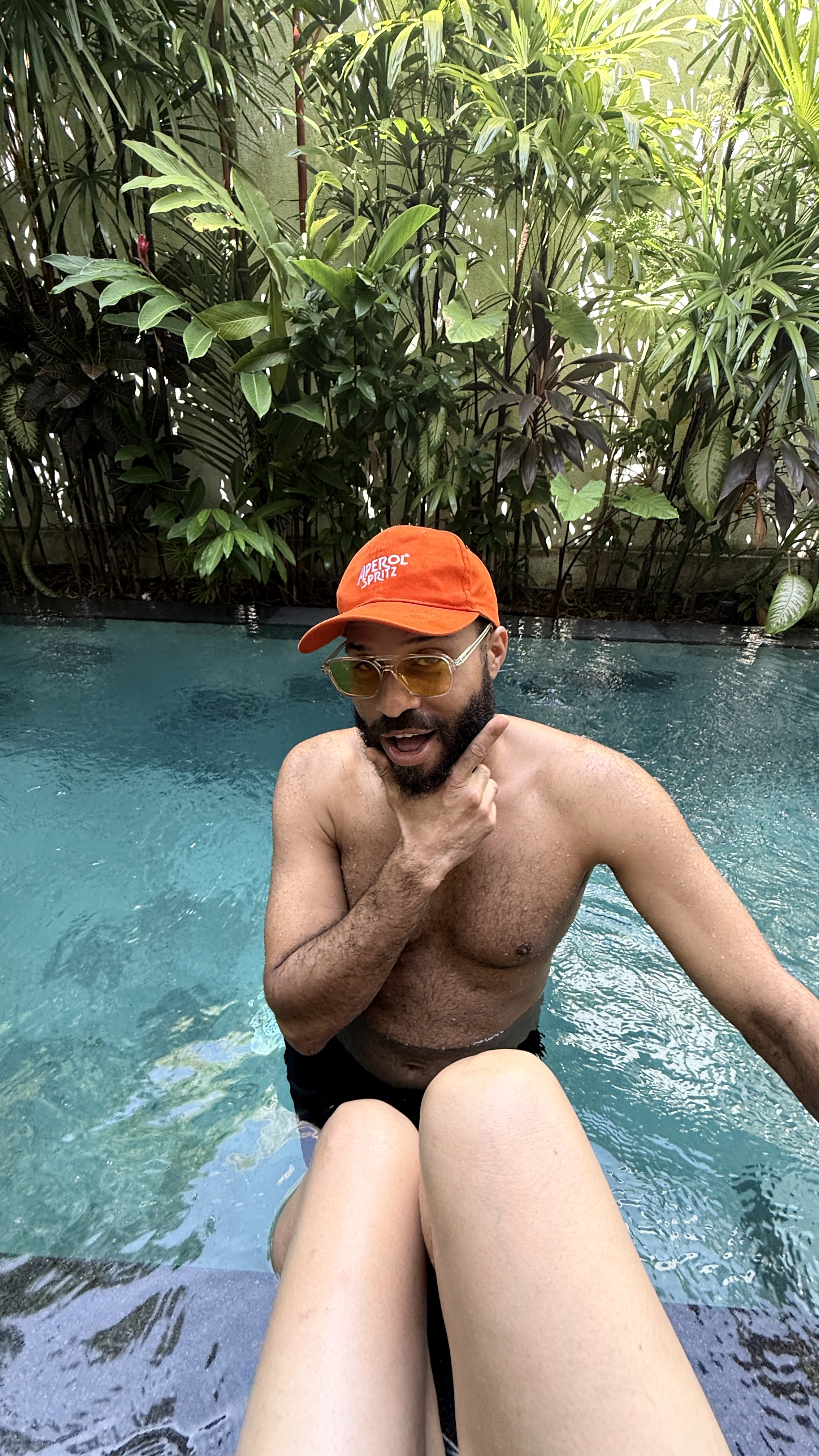 Taylor striking a confident pose in the pool, wearing an orange cap and sunglasses.